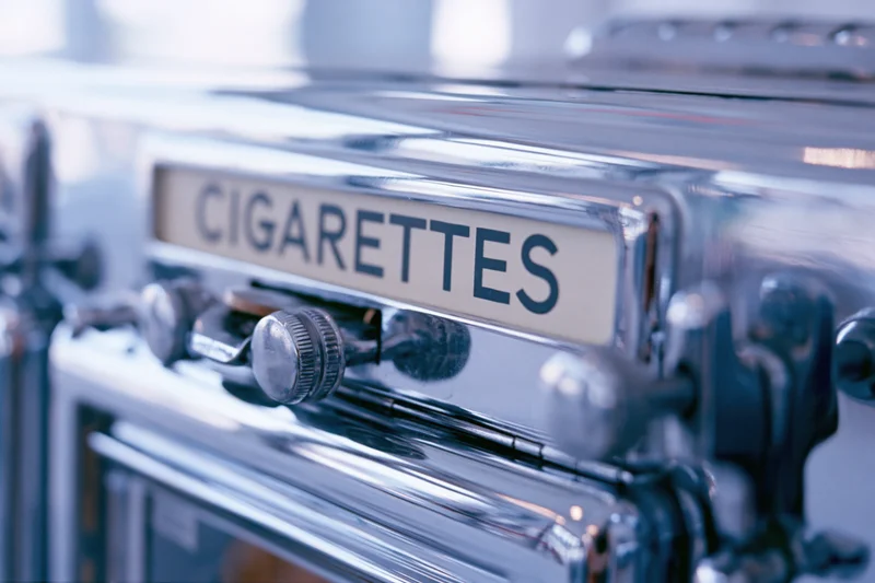 Close-up of a vintage chrome cigarette vending machine with a label and coin slot