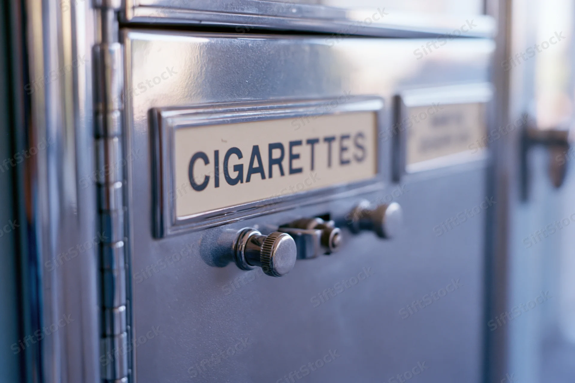 Close-up of a vintage chrome cigarette vending machine showing the labeled slot and coin mechanism