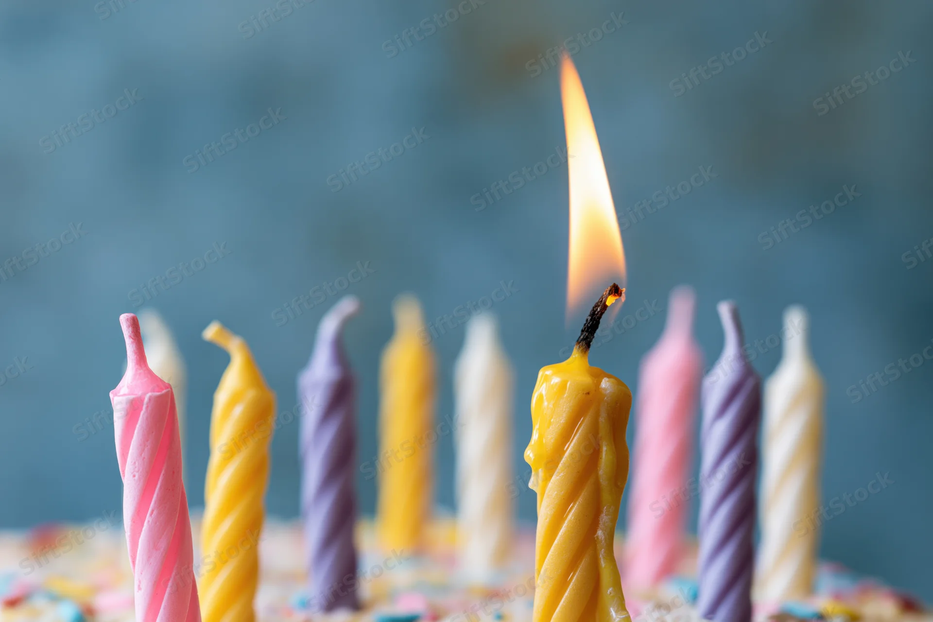 Close-up of colorful twisted birthday candles on a cake with one lit flame against a blue background