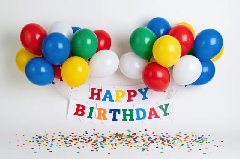 Colorful balloons clustered in two bunches flanking a happy birthday banner with confetti on white background