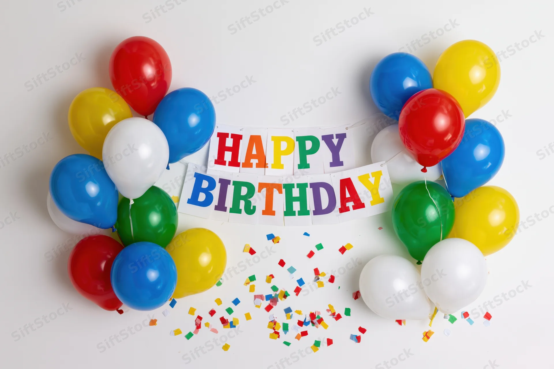 Colorful balloons and a happy birthday banner arranged on a white surface with scattered confetti