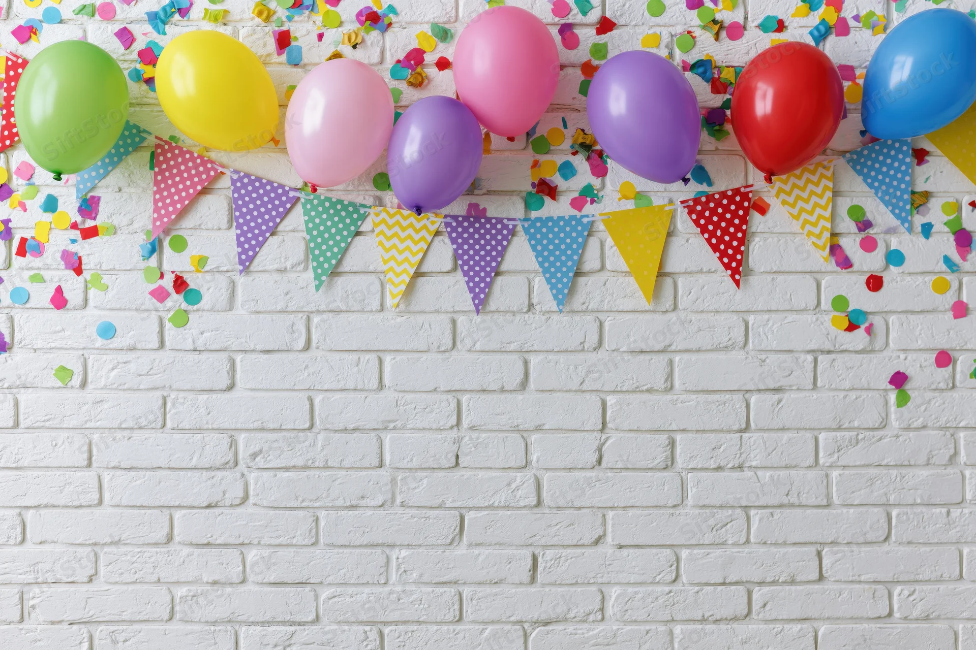 Colorful party decorations with balloons and bunting on a white brick wall