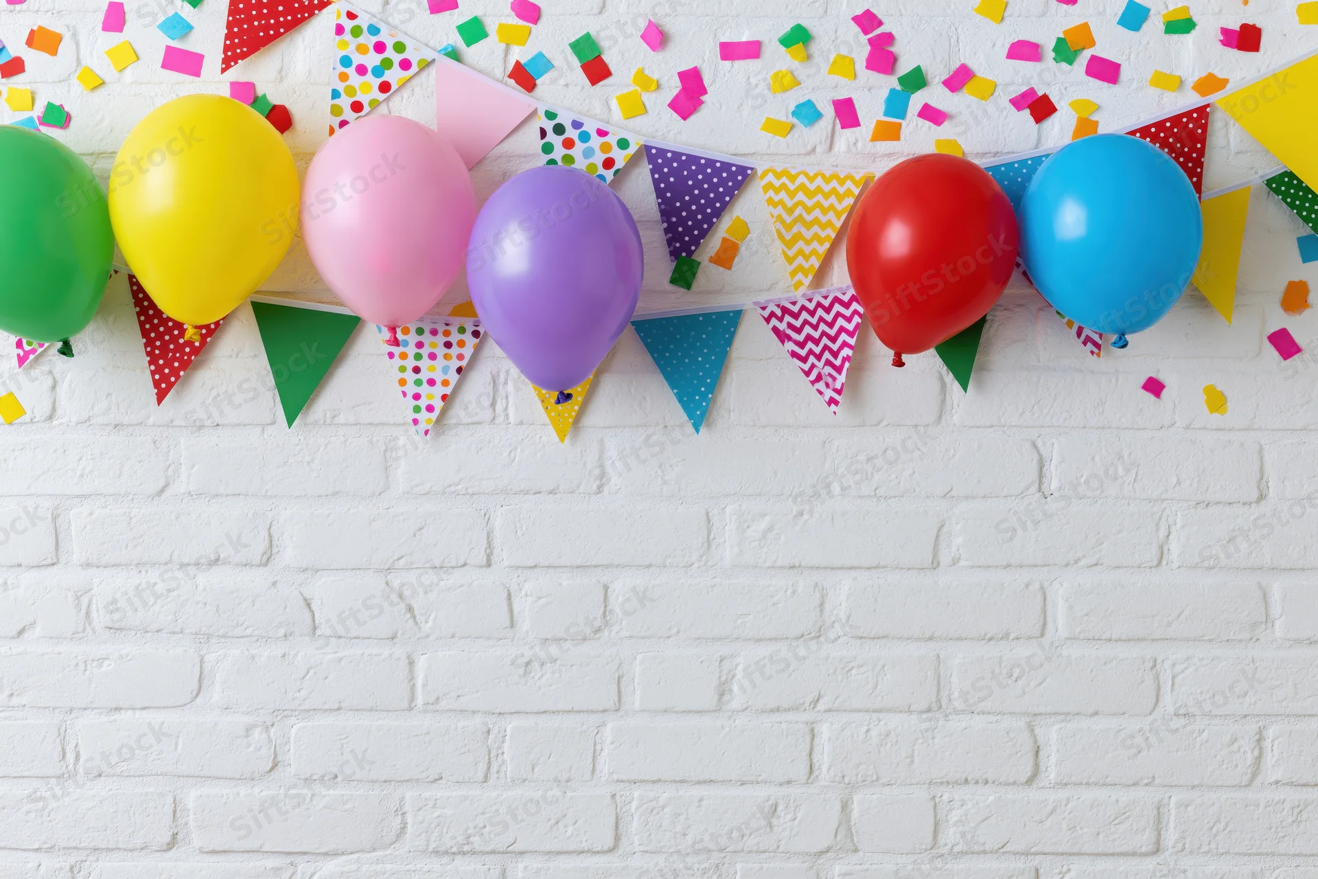 Colorful balloons and patterned banner with confetti on white brick wall