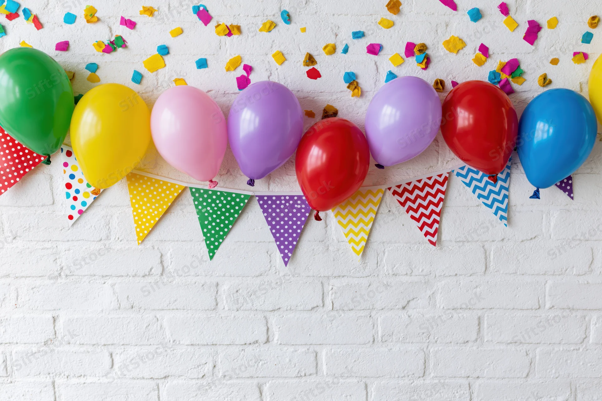Colorful balloons and patterned banner with confetti on white brick wall