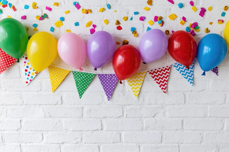 Colorful balloons and patterned banner with confetti on white brick wall