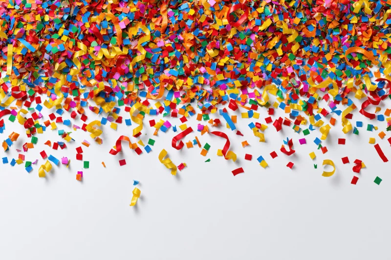 Colorful paper confetti and curled ribbon streamers scattered across white surface with copyspace