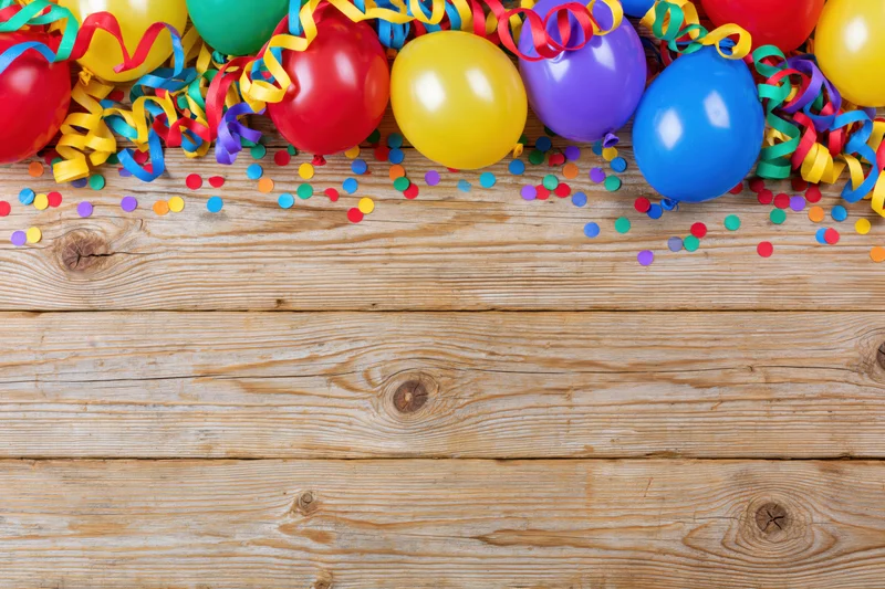 Colorful party balloons and streamers with confetti arranged along the top of a wooden table surface