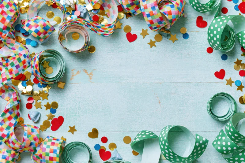 Colorful party streamers and confetti arranged around a light blue wooden surface with copyspace in center