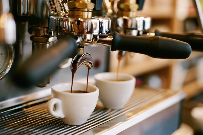 Espresso machine brewing coffee into two white cups on a metal drip tray in a cafe