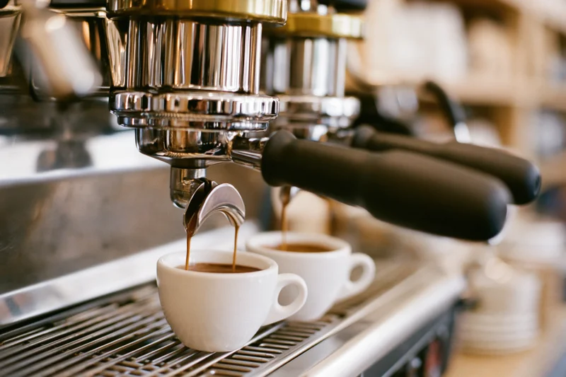 Espresso machine brewing coffee into white cups on a commercial countertop