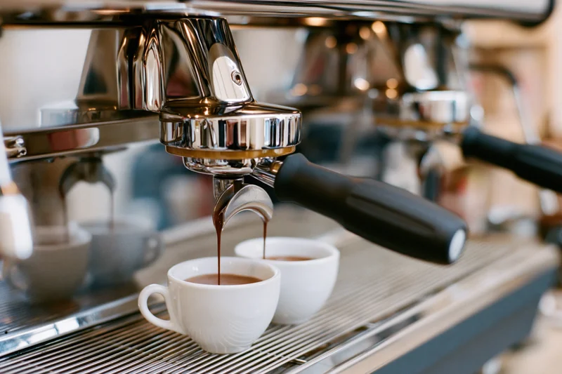 Espresso machine brewing coffee into two white cups on a metal counter