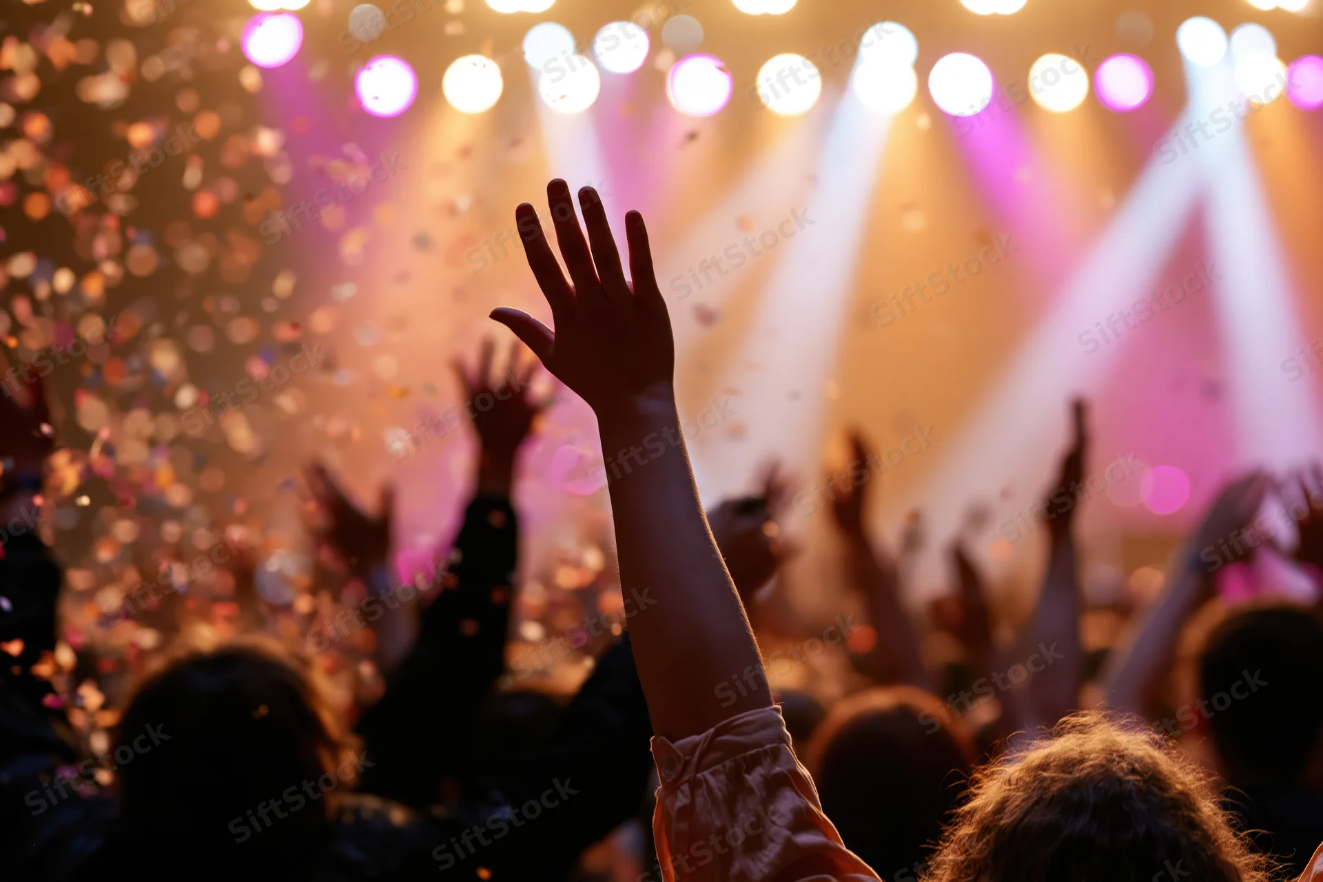 Crowd at concert raising arms toward stage with confetti and stage lights