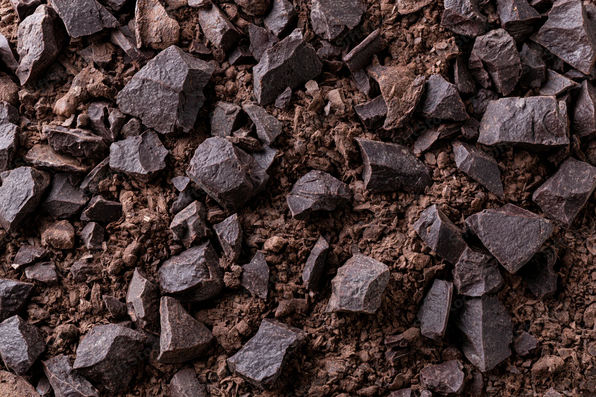 Crushed dark chocolate pieces and fine cocoa shavings spread across a textured surface