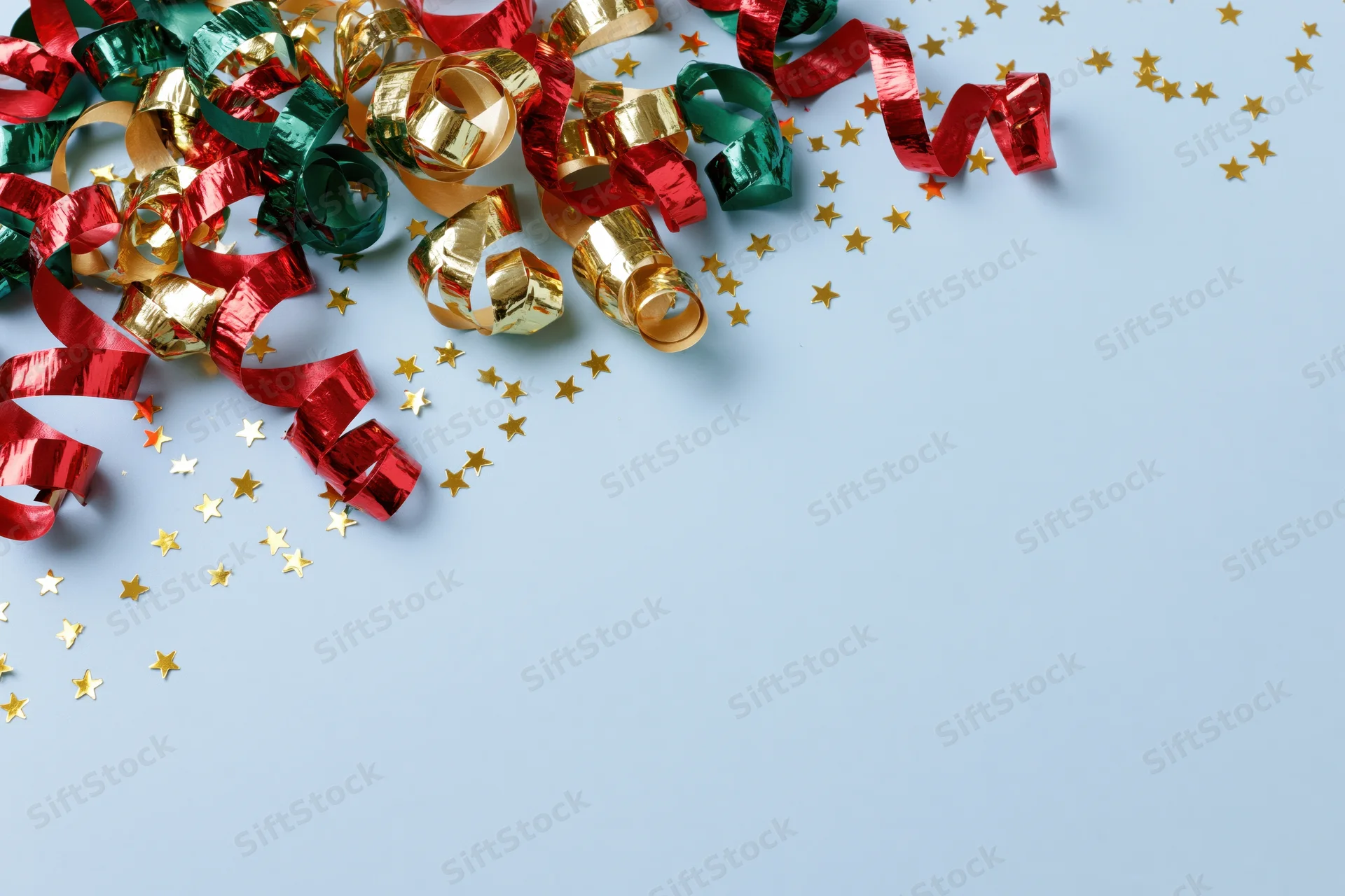 Curled metallic streamers and star-shaped confetti scattered on a light blue surface with copyspace