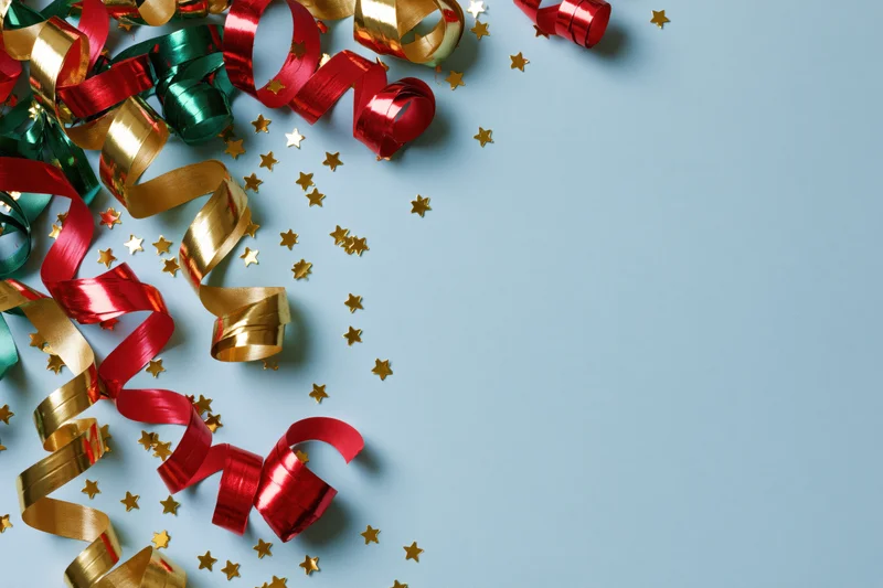 Curled metallic streamers and star-shaped confetti scattered on a blue surface with copyspace
