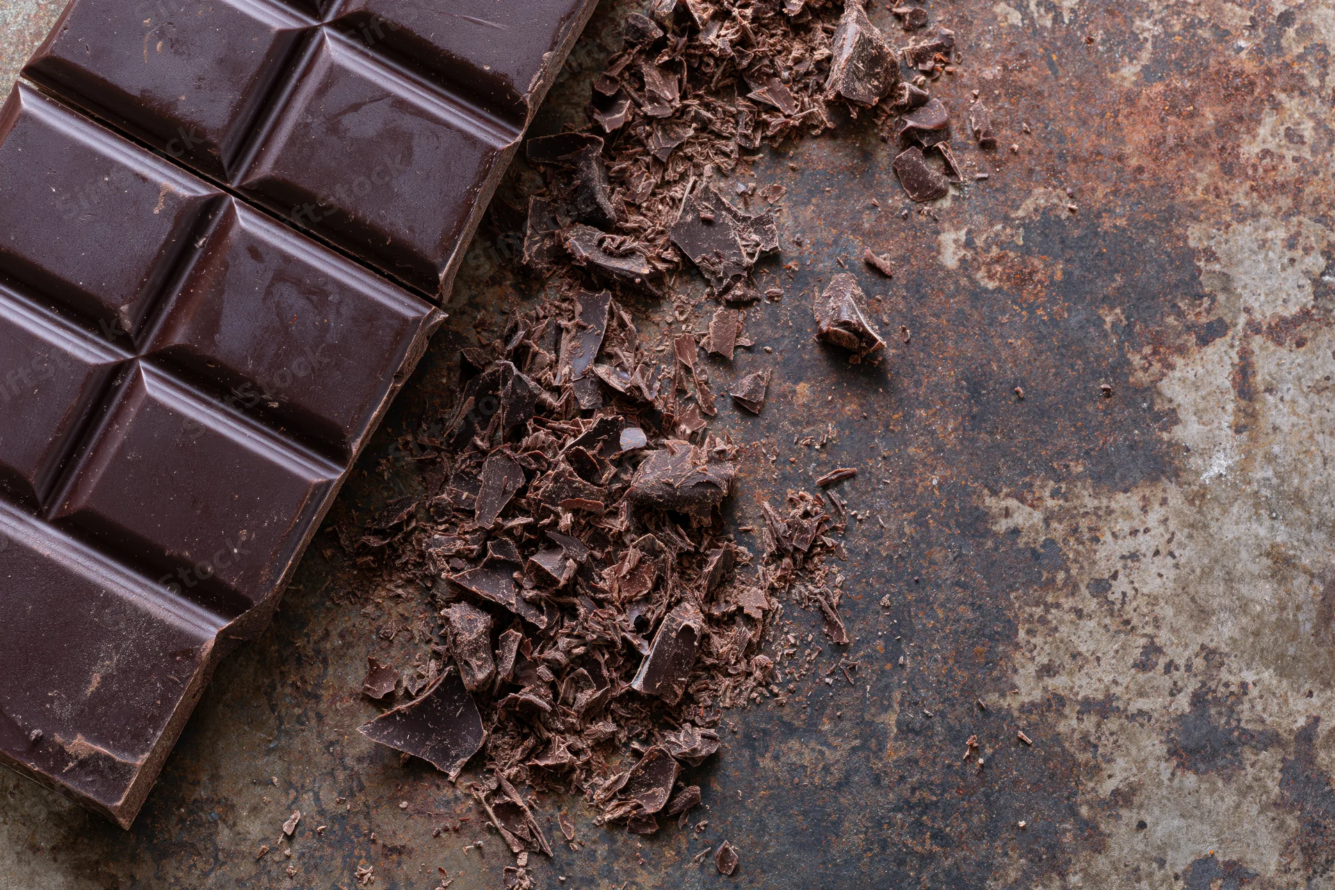 Dark chocolate bar broken into squares and crumbled pieces on a rusty metal surface