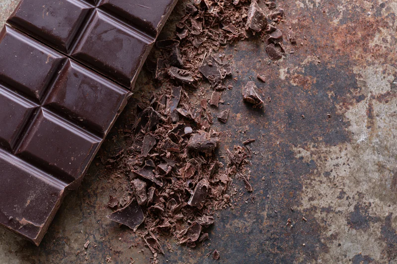Dark chocolate bar broken into squares and crumbled pieces on a rusty metal surface