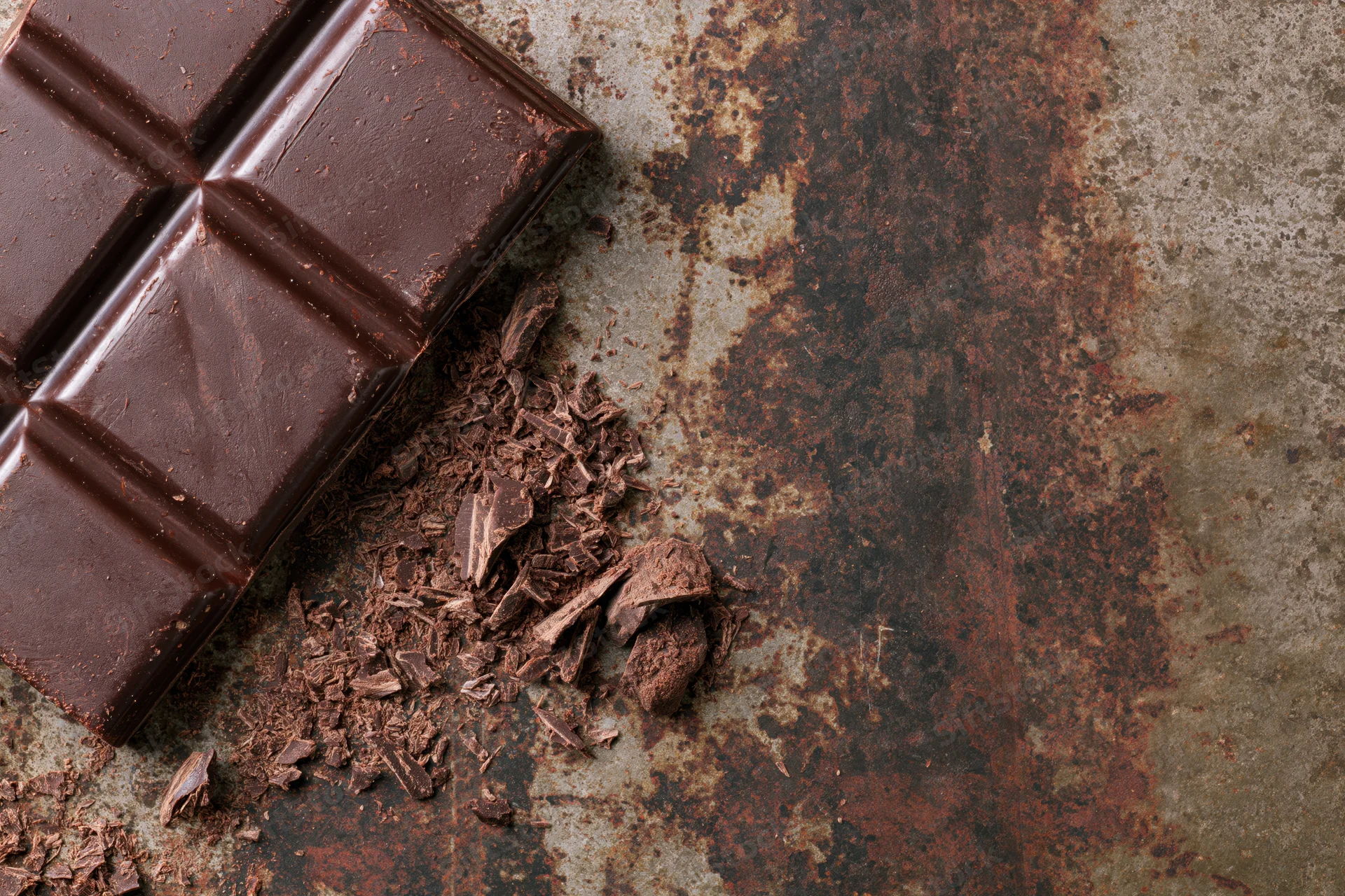 Dark chocolate bar broken into squares and crumbs on a rusted metal surface