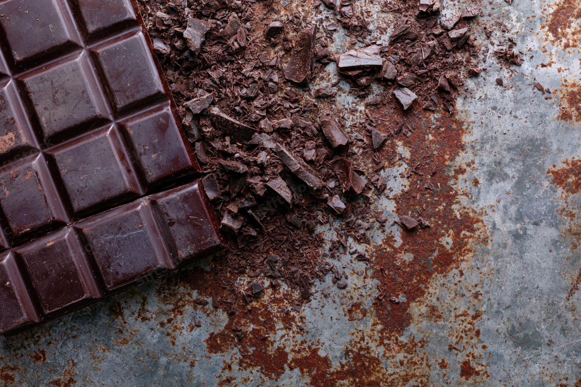Dark chocolate bar broken into squares and crumbs on a rusted metal surface