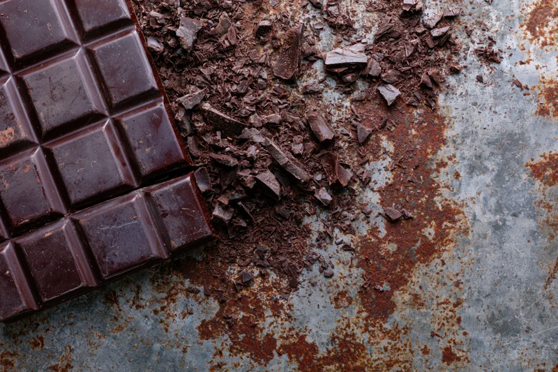 Dark chocolate bar broken into squares and crumbs on a rusted metal surface