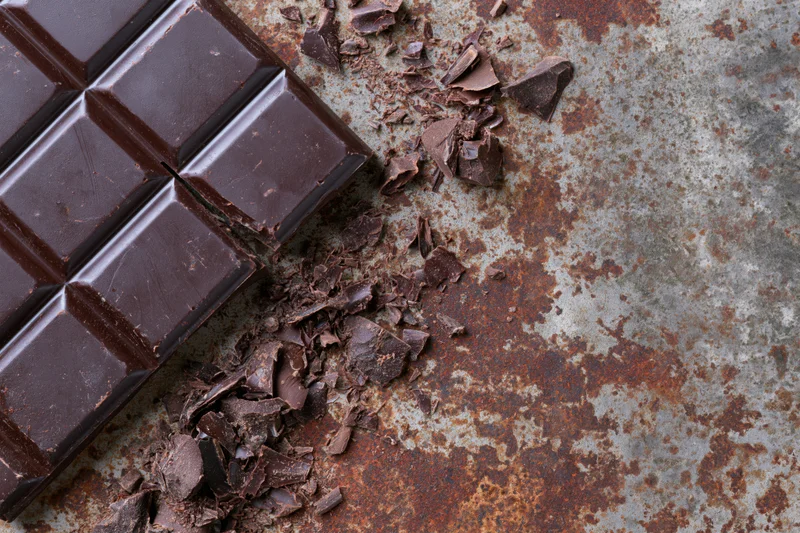 Dark chocolate bar broken into squares and scattered pieces on a rusted metal surface
