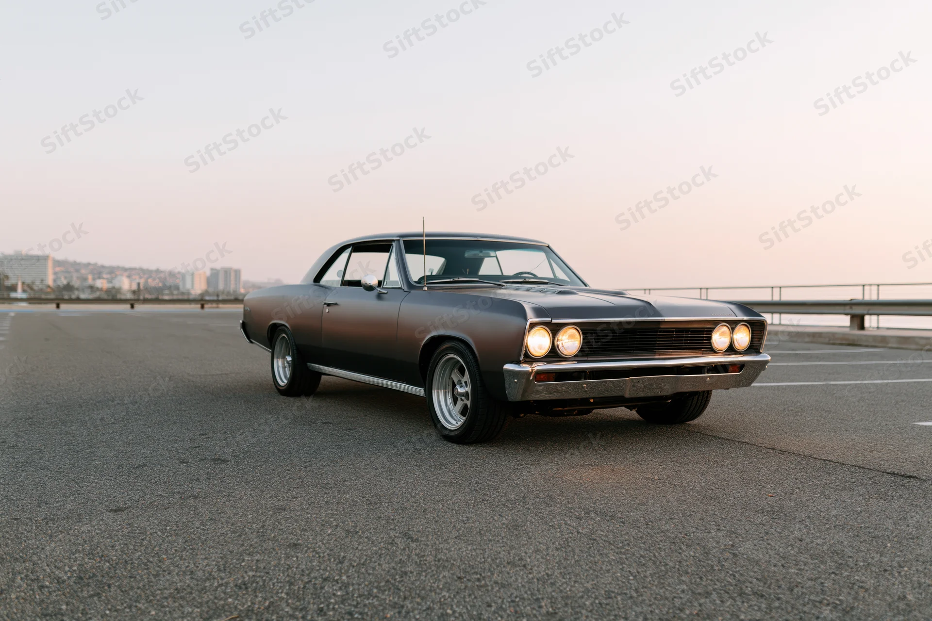 Dark grey 1960s american muscle car parked on empty asphalt road at sunset