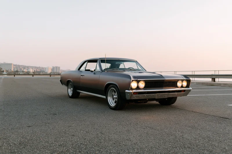 Dark grey 1960s american muscle car parked on empty asphalt road at sunset