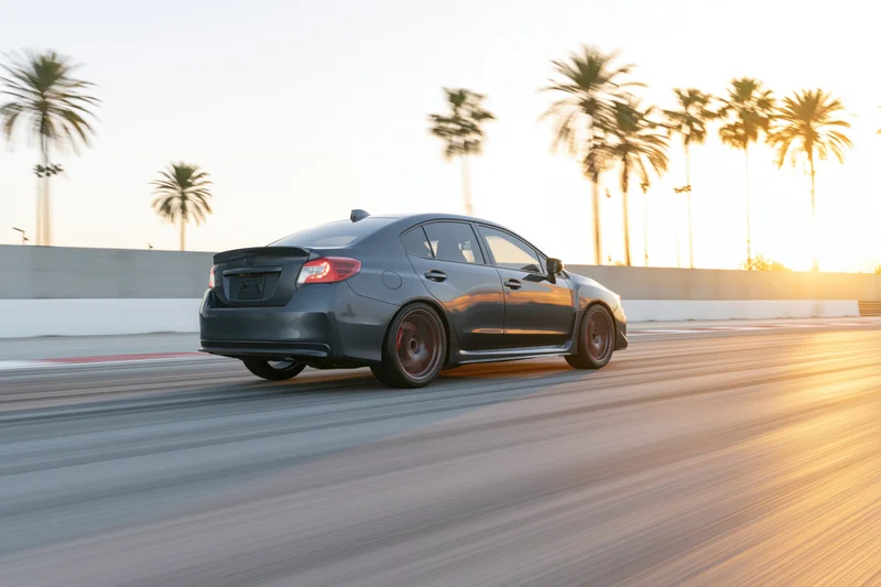 Dark grey sport sedan driving at speed on a smooth race track with palm trees in the background at sunset
