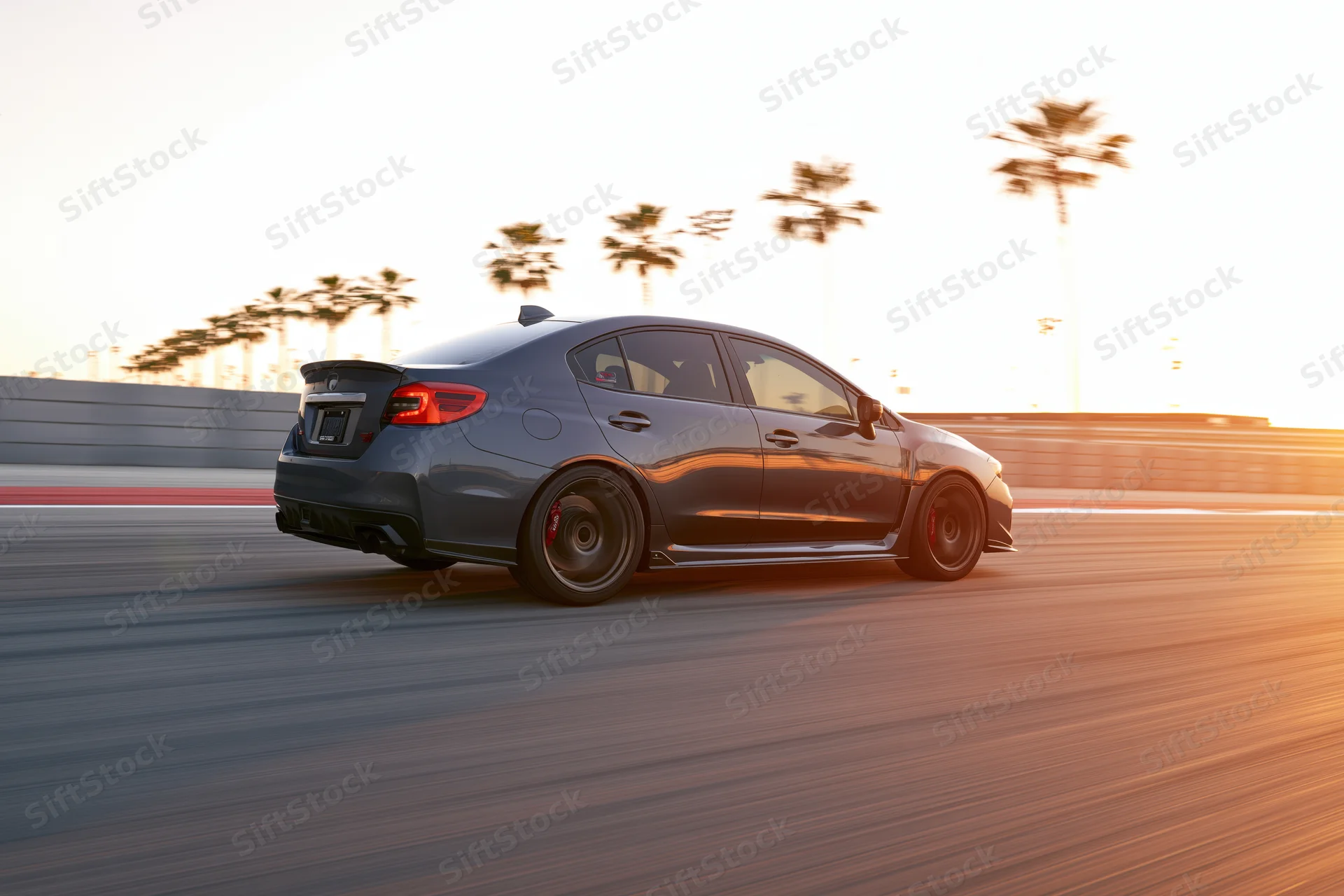 Dark grey sport sedan driving at speed on a smooth race track with palm trees and sunset light