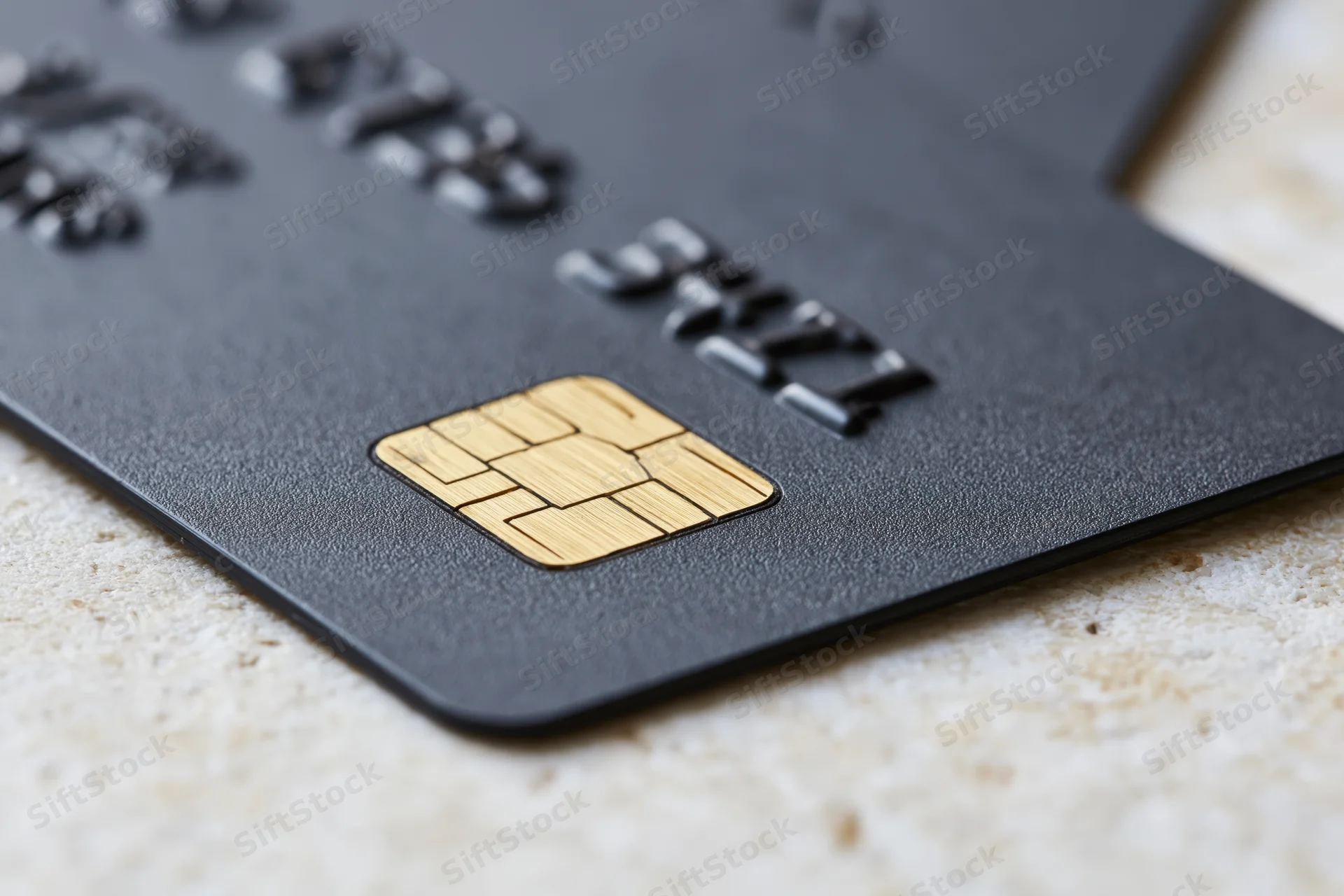 Closeup of a black matte credit card with gold chip resting on a light stone surface