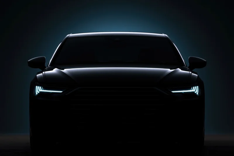 Dark sedan silhouetted head-on with glowing led headlights in a studio setting