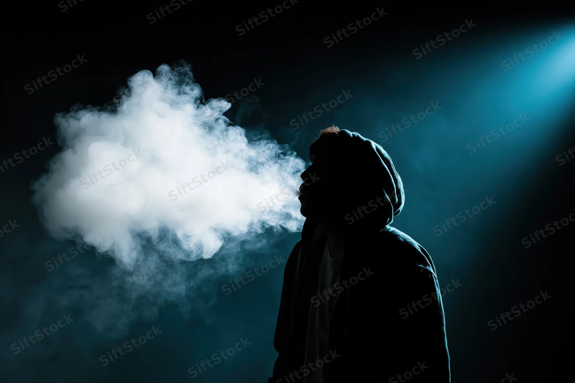 Hooded figure exhaling a large cloud of vapor in a dark blue-lit space