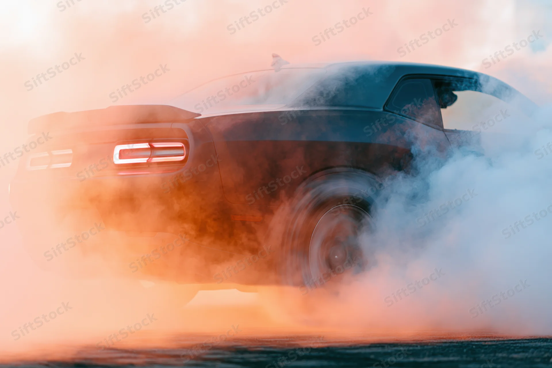 Dark sports car performing burnout on race track with smoke and motion blur at dusk