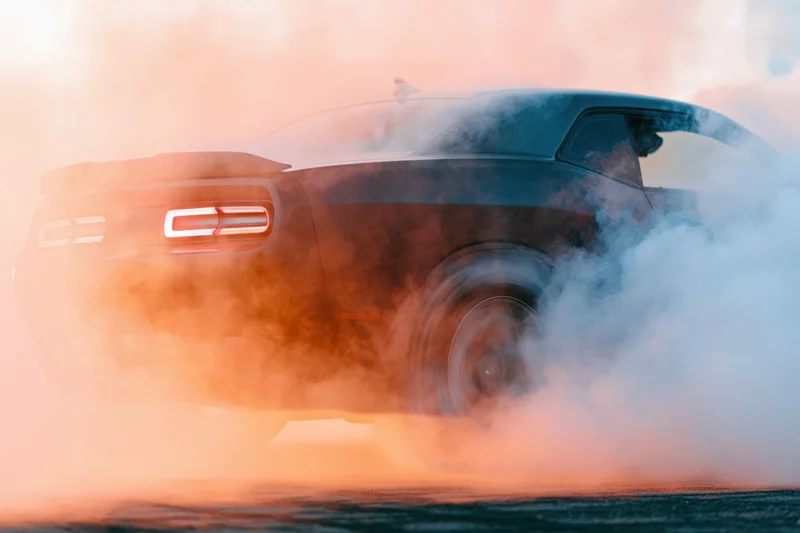 Dark sports car performing burnout on race track with smoke and motion blur at dusk