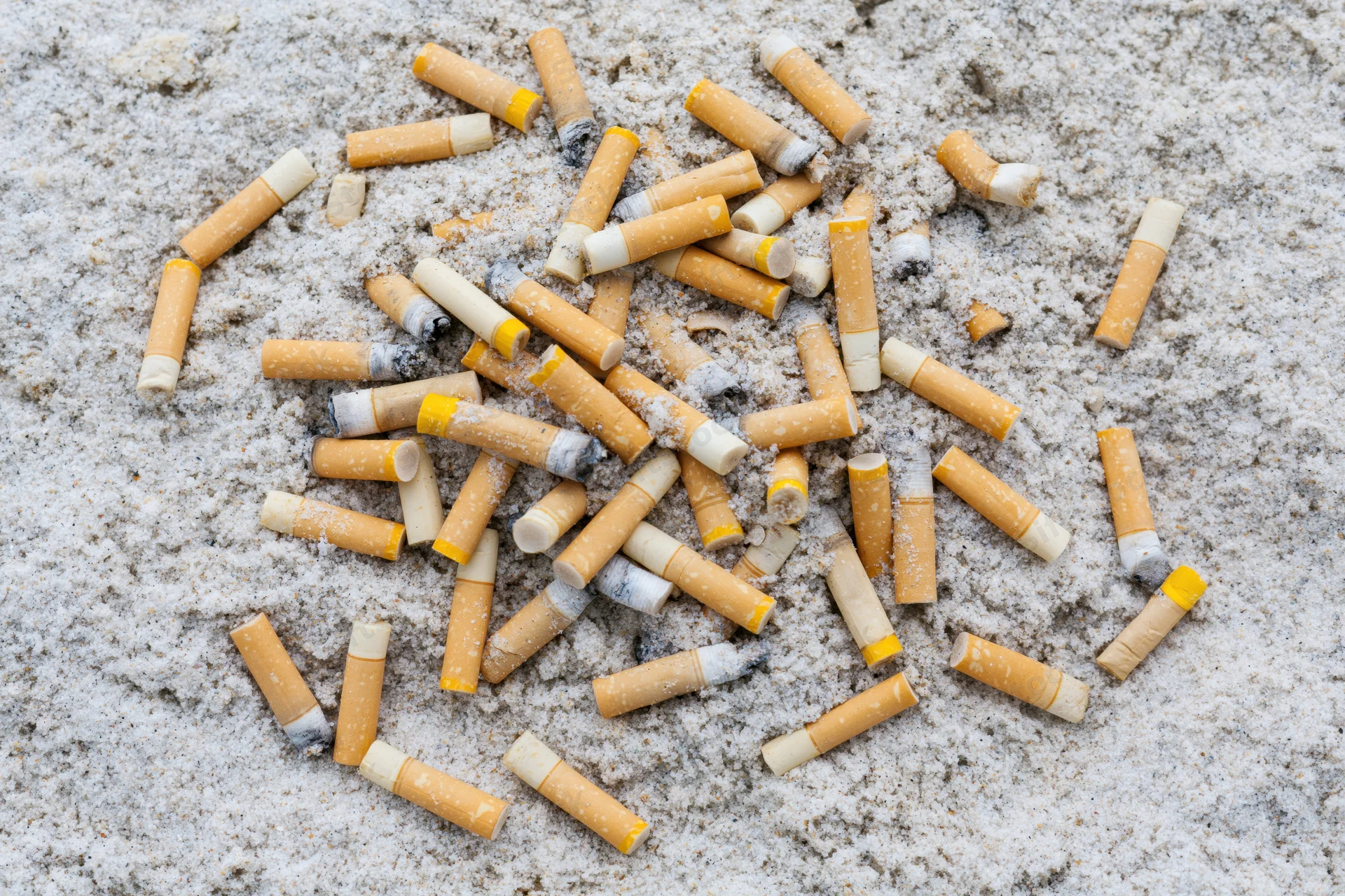Cigarette butts scattered and half-buried in sand on a beach