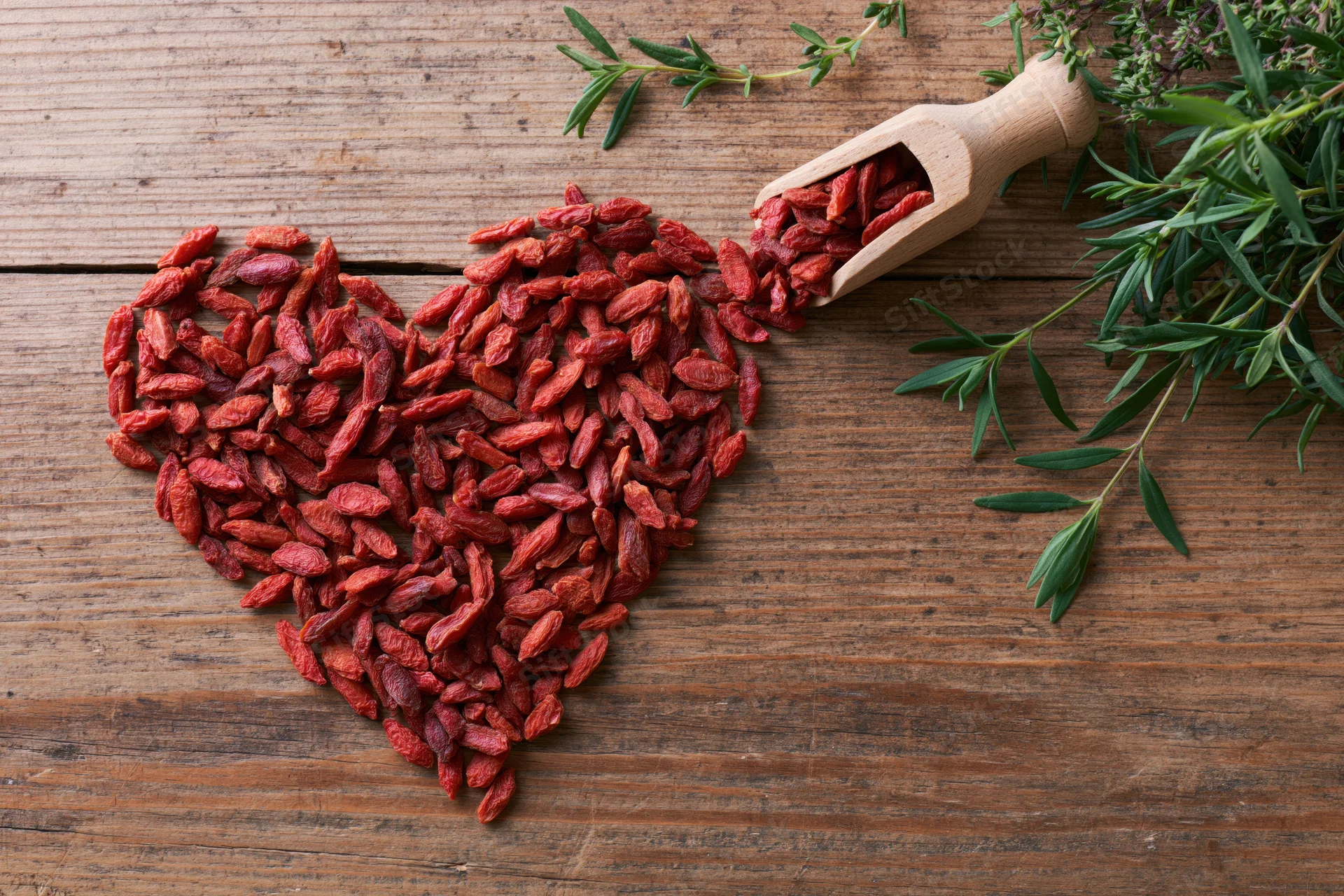 Dried goji berries arranged in heart shape on rustic wooden table with wooden scoop and fresh thyme sprigs