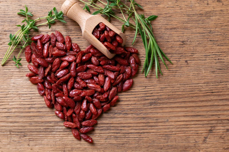 Dried goji berries arranged in heart shape on wooden surface with herbs