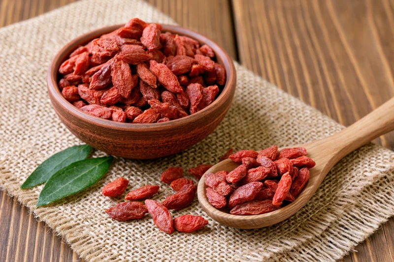 Dried goji berries in a rustic clay bowl and wooden spoon on burlap cloth over wood surface