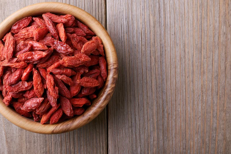 Dried red goji berries in a round wooden bowl on a rustic wooden surface