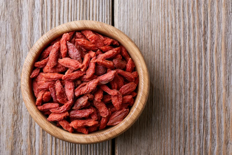 Dried red goji berries in a round wooden bowl on a rustic wooden surface