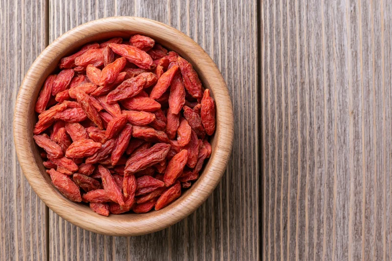 Dried red goji berries in a round wooden bowl on a rustic wooden surface