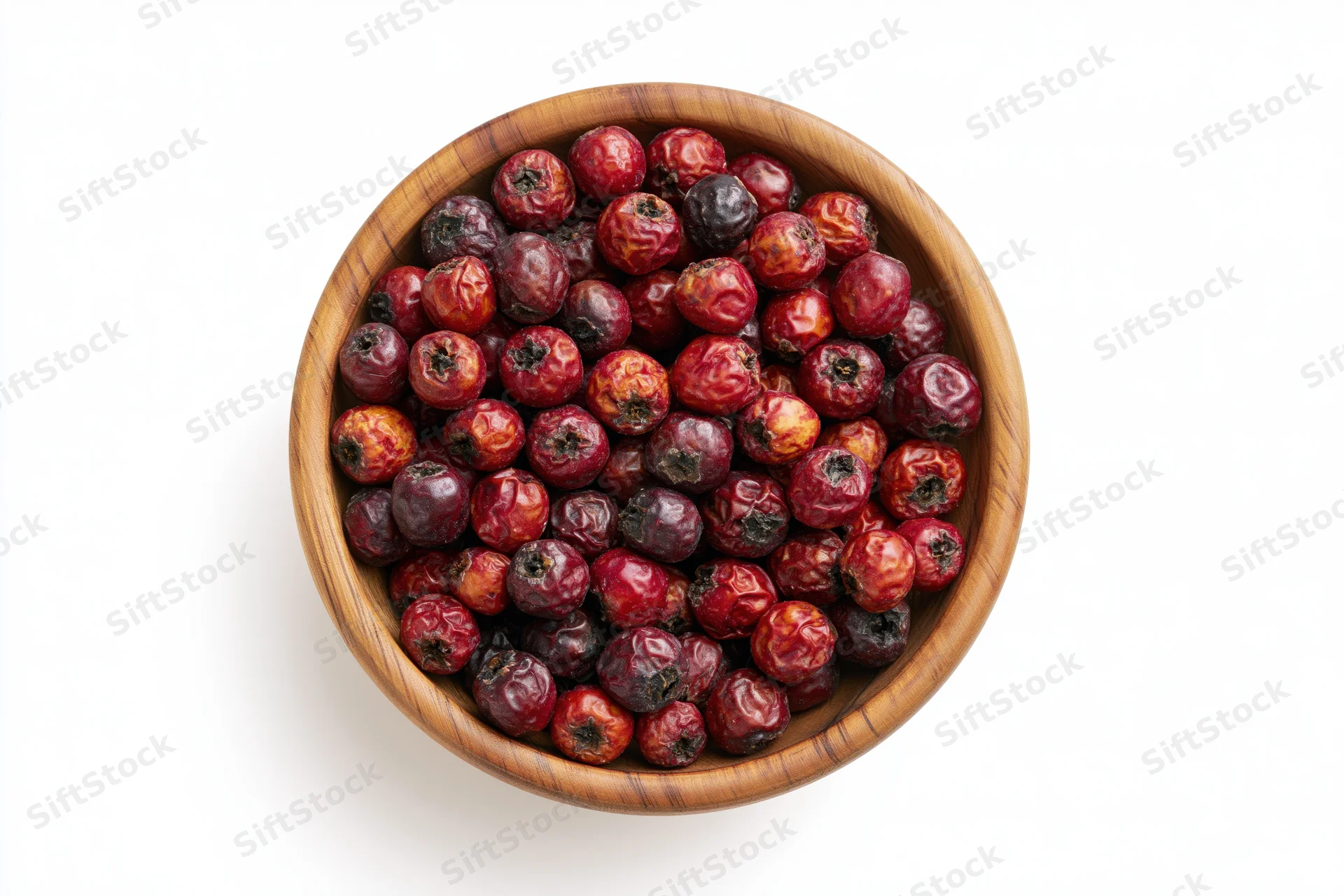 Dried hawthorn berries in a small wooden bowl on white background