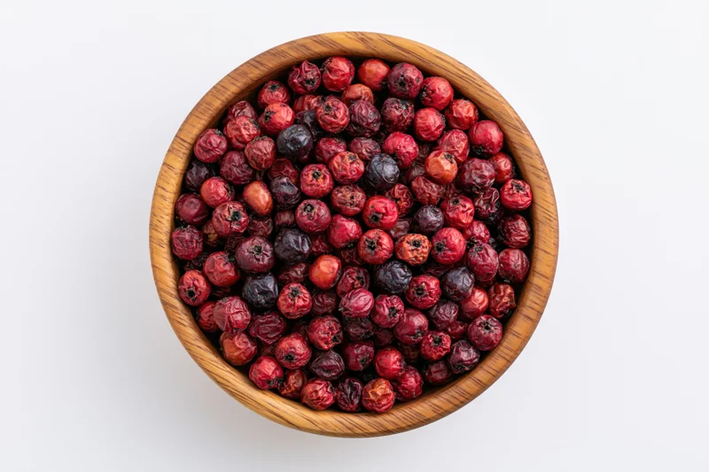 Dried hawthorn berries in a wooden bowl on white background