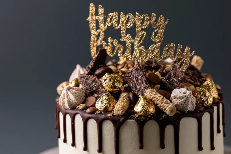 Chocolate drip birthday cake topped with gold glitter topper and assorted candies