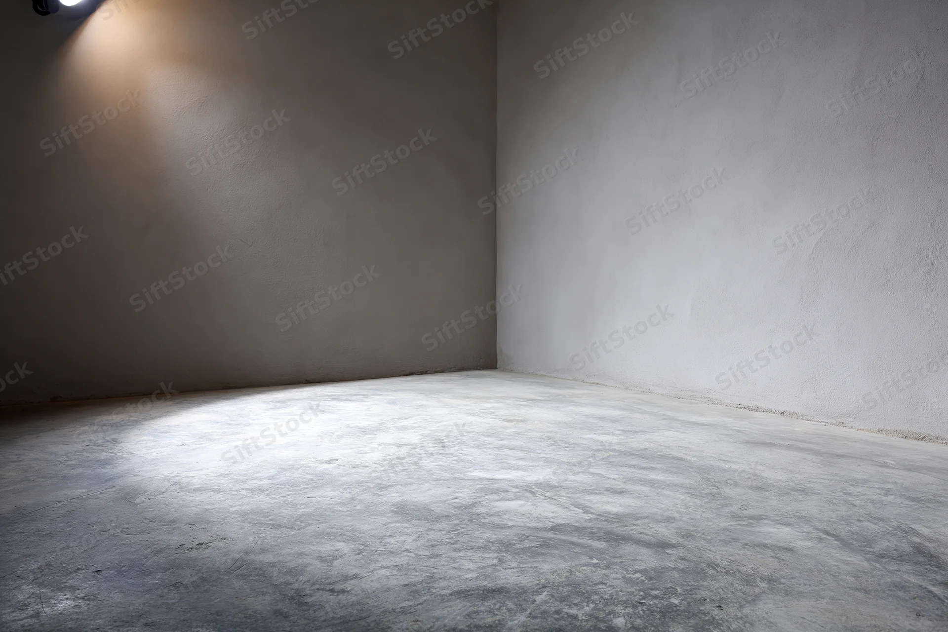 Empty studio interior with concrete floor and grey walls lit by spotlight