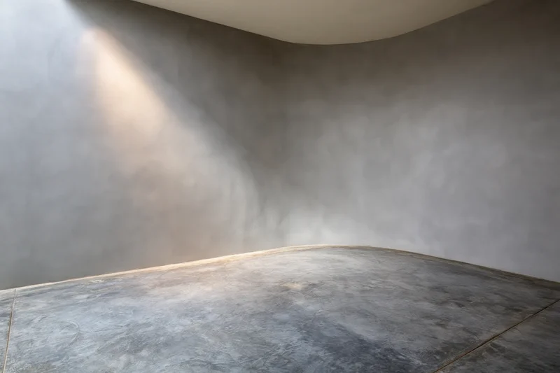 Empty studio interior with curved concrete walls and floor, lit by natural light from above