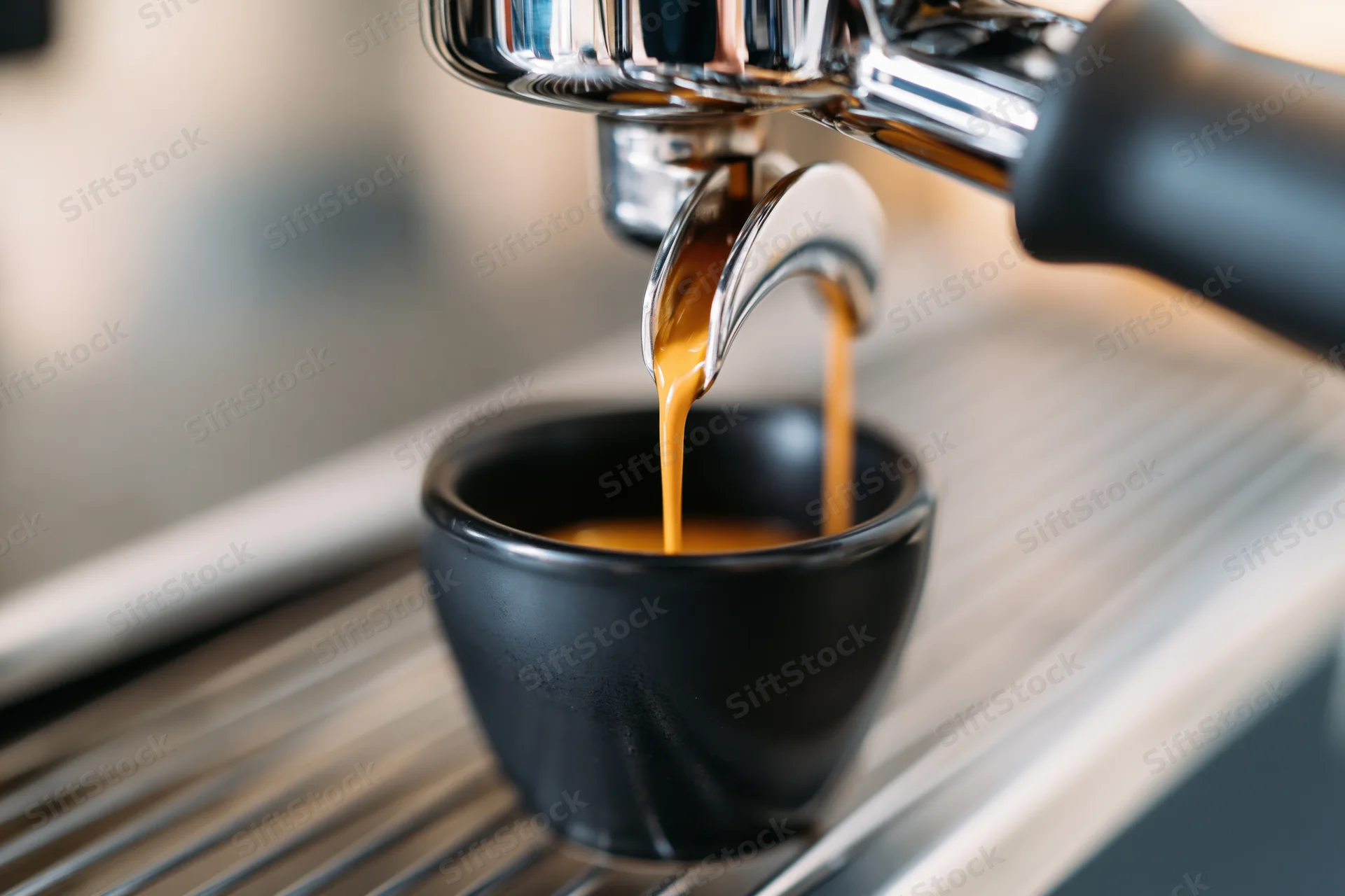 Espresso machine portafilter pulling a shot into a black cup on a metal drip tray