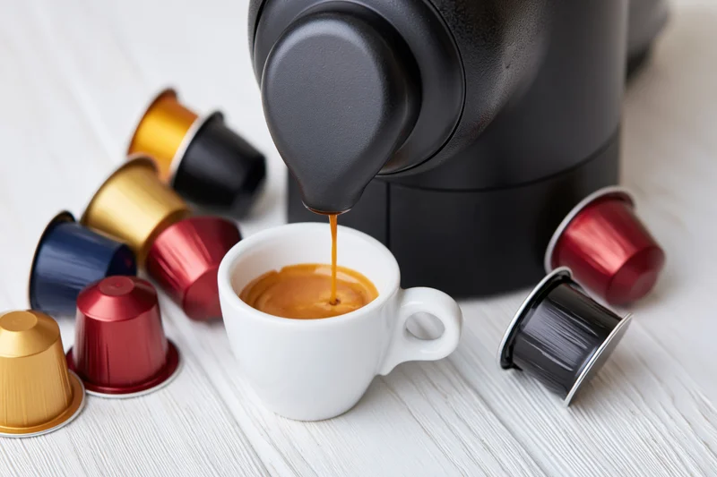 Espresso machine pouring coffee into a white cup surrounded by colorful pods on a wooden surface