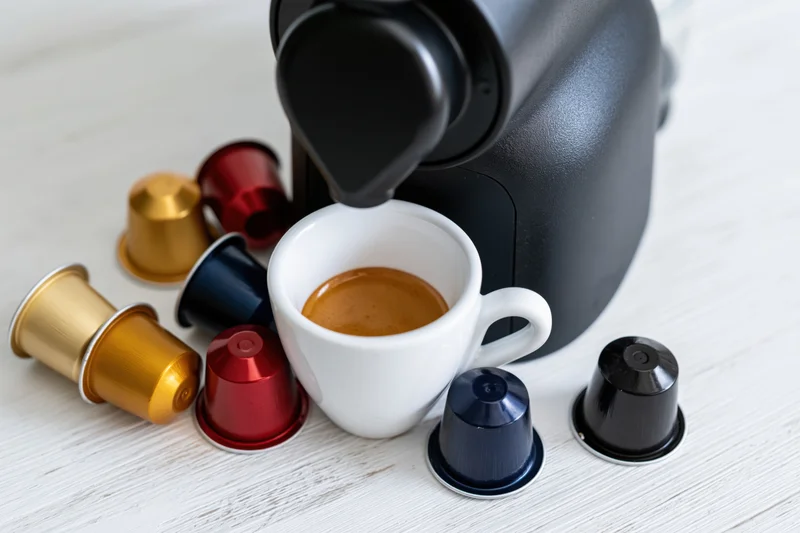 Espresso machine dispensing coffee into a white cup surrounded by colorful pods on a countertop