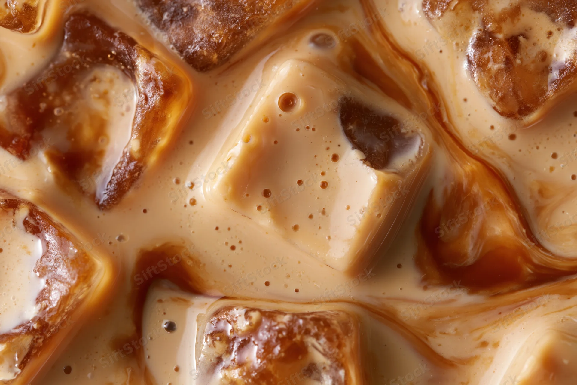 Closeup of iced coffee surface with floating ice cubes and creamy swirls